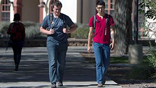 Two students are on campus talking and walking towards the camera.